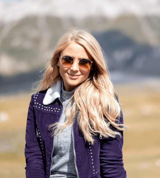 Portrait of Aprisa Thompson outdoors wearing sunglasses with mountains in the background, team member photo in the Layout 3 team section demo